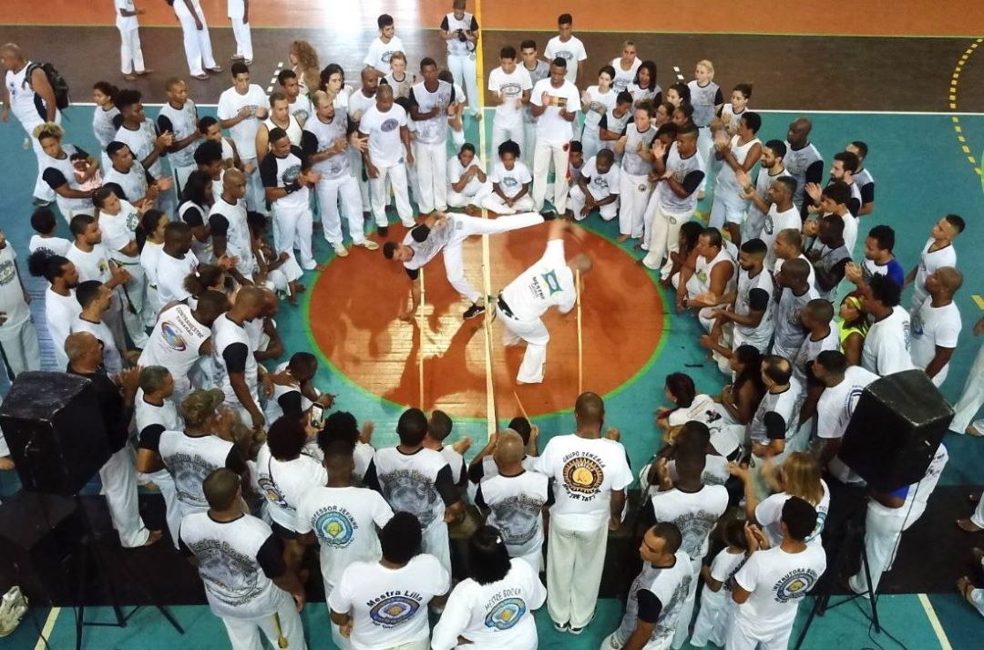 High angle shot of a large circle of people with two people in the middle, one dodging as the other kicks.